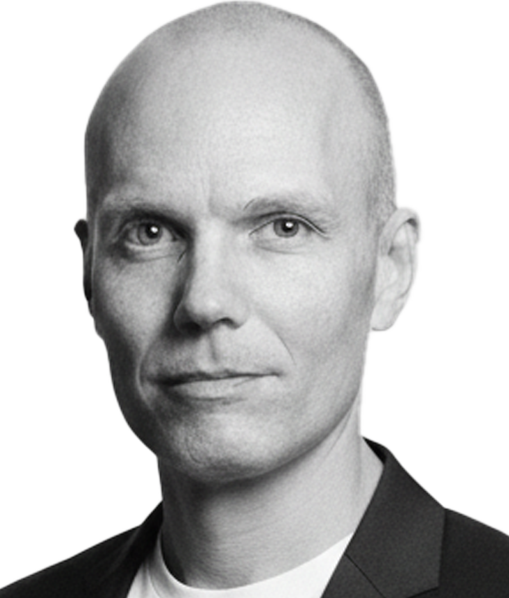 A black and white headshot of a man with a shaved head wearing a suit